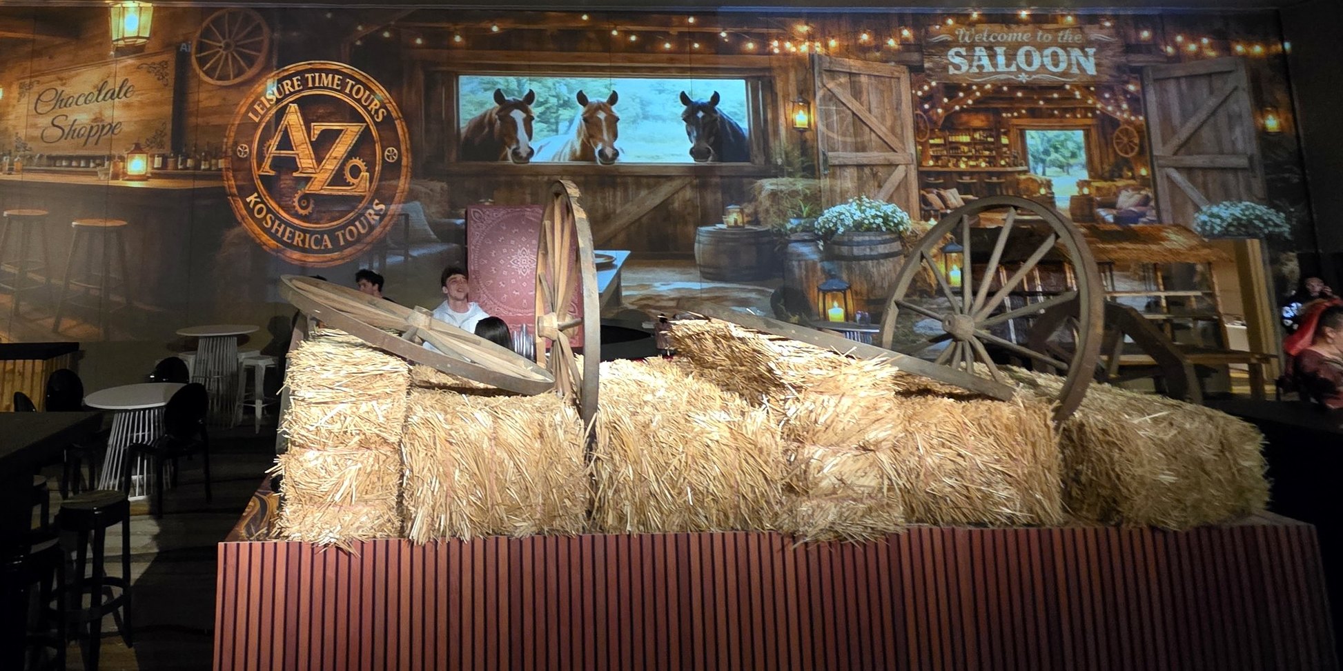 The whole room: the barn and saloon projected across the wall, hay bales and the wagon wheel in front, the tables lit