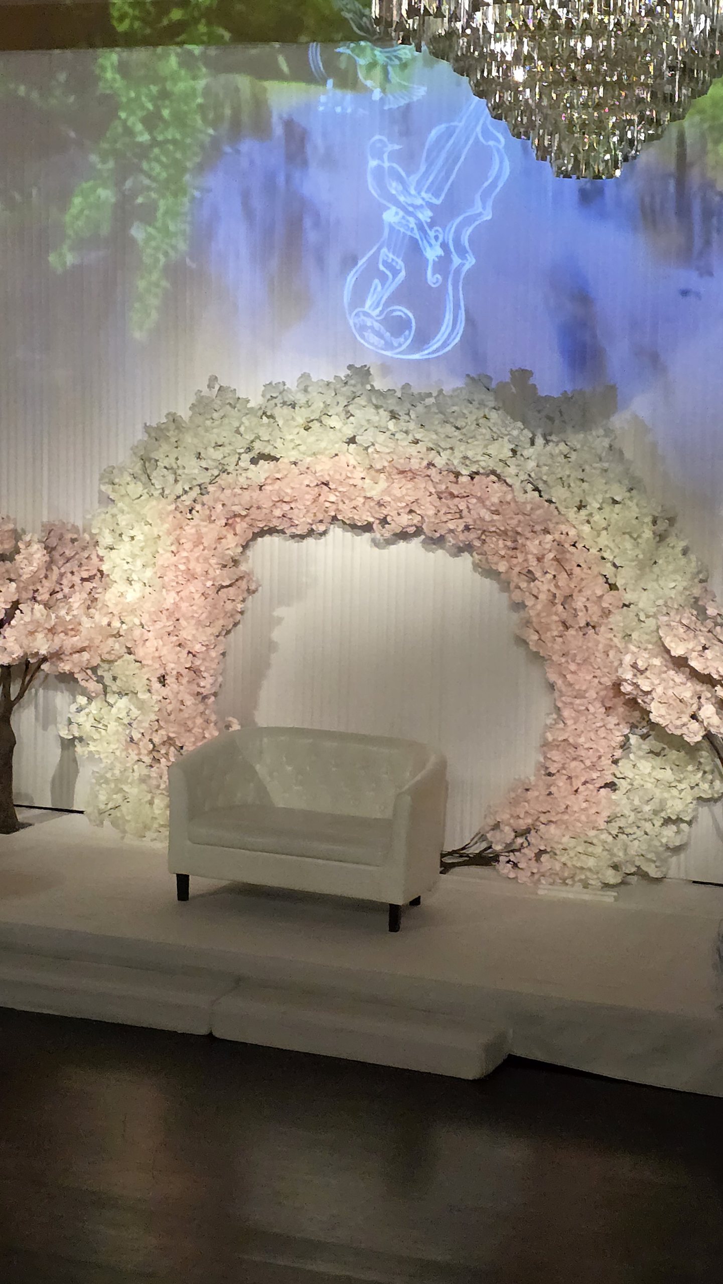 The blossom arch for the couple, a violin drawn in light on the wall above it