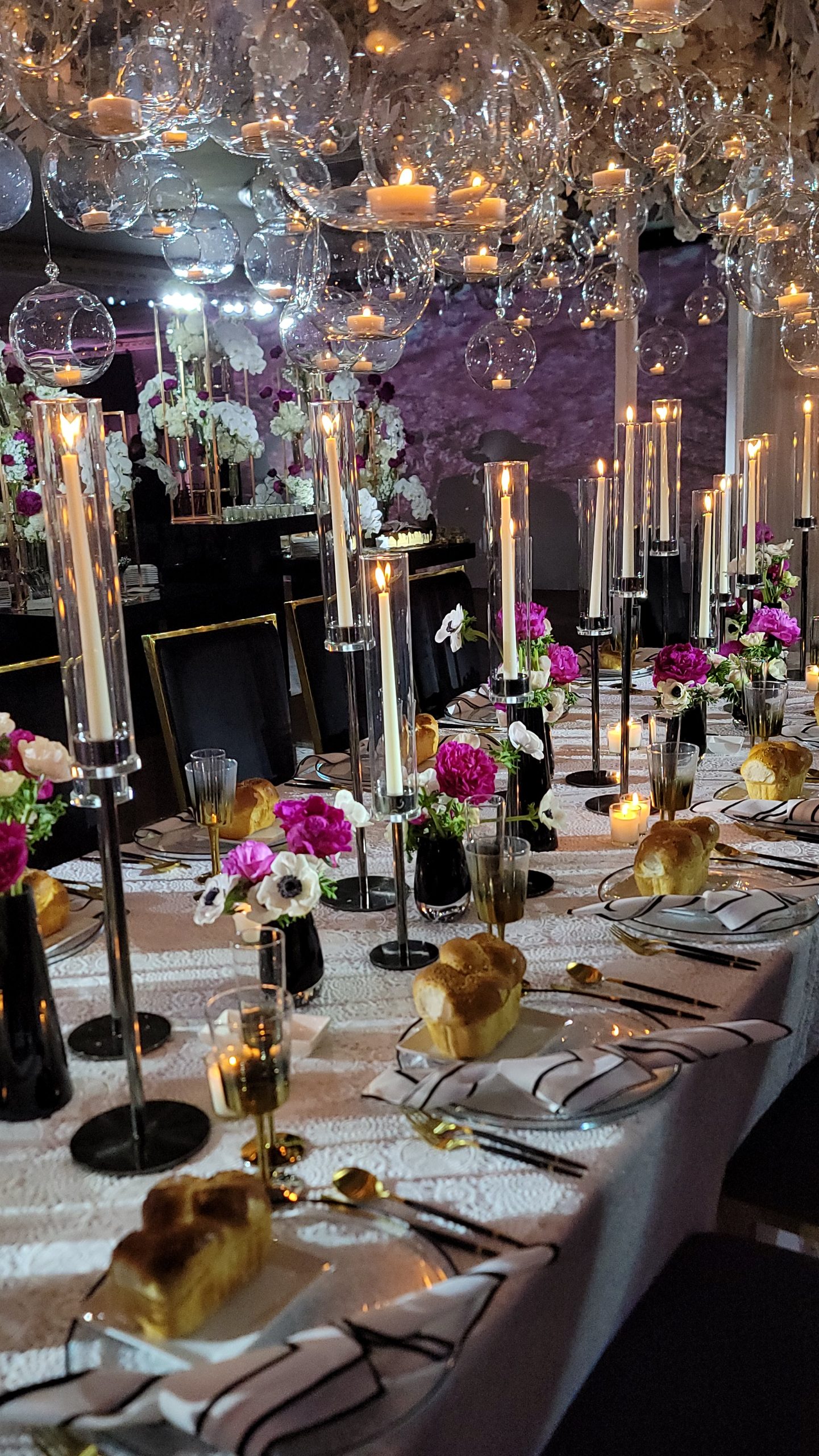A long table under glass orbs and tapers, fuchsia peonies and challah at every place