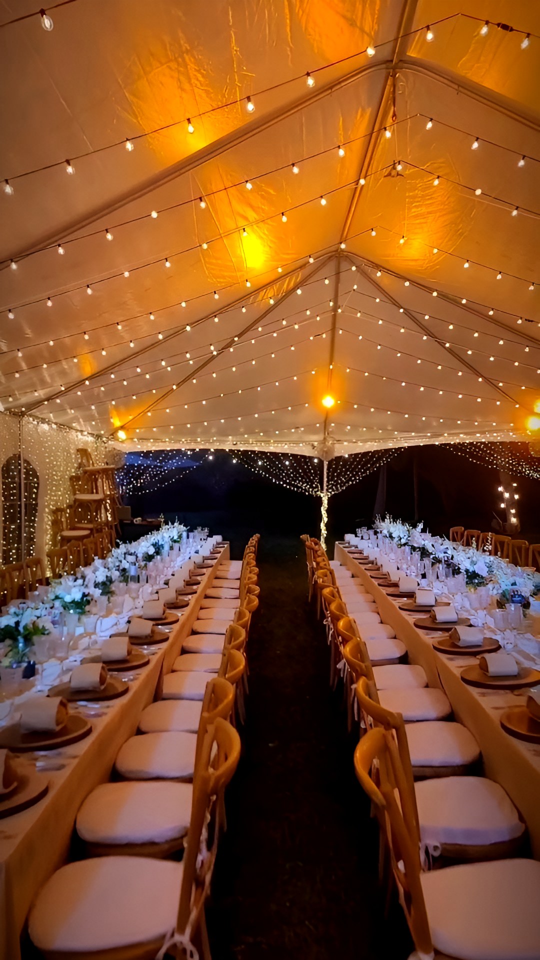 A tent at night: string lights over long white tables
