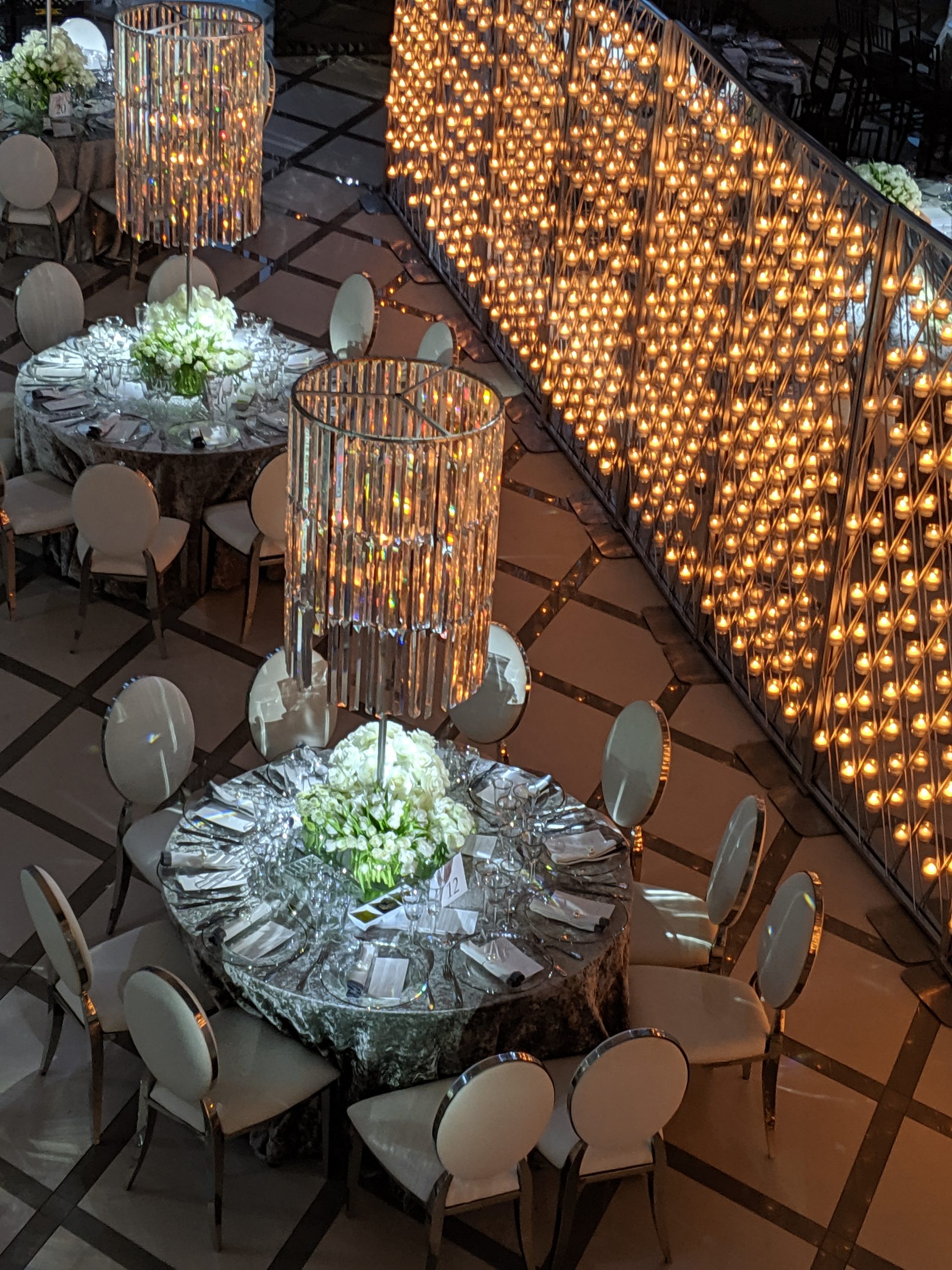 The candle wall down the whole length of the room, the round tables set in white beside it, a crystal chandelier above