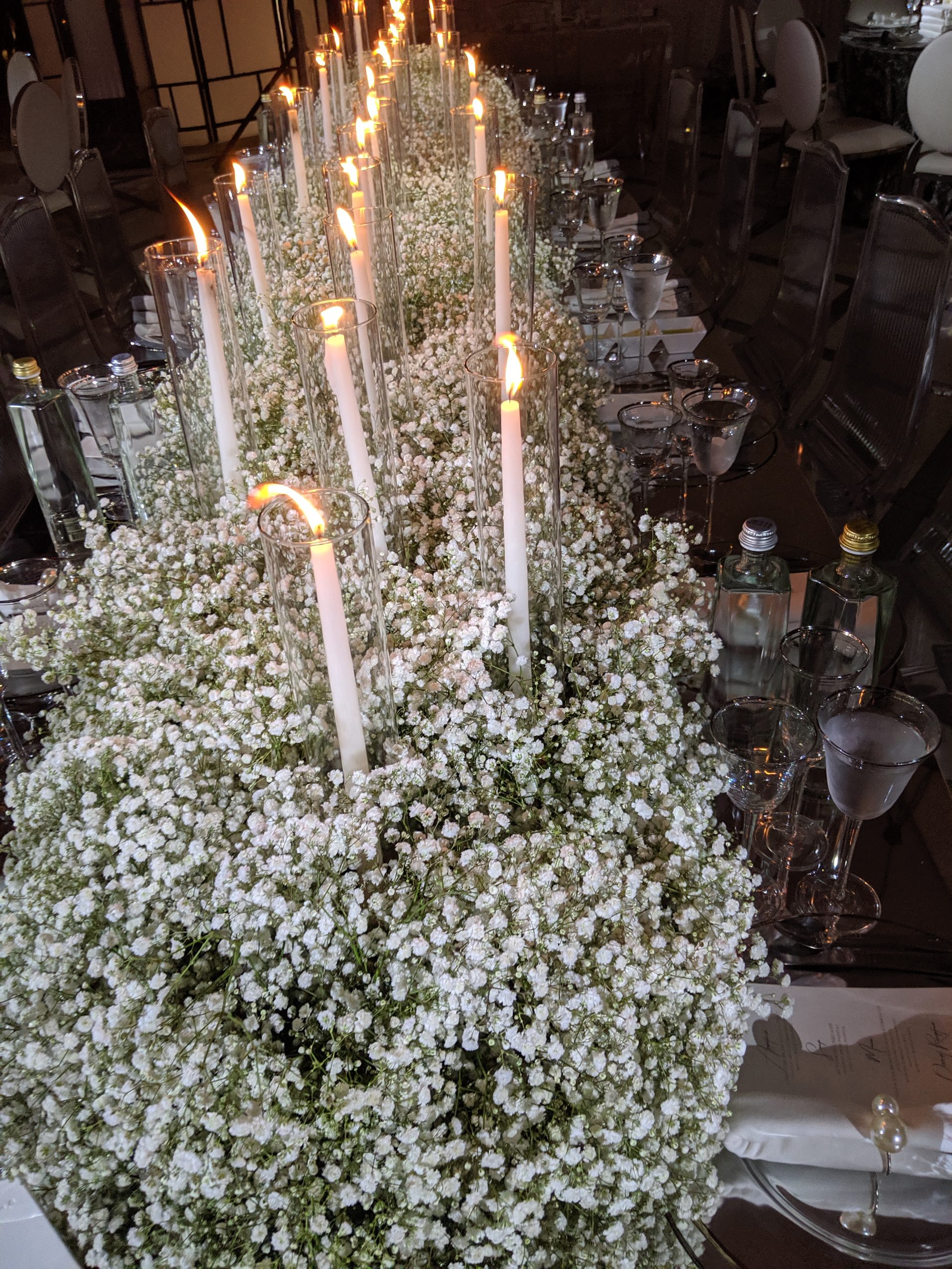 A mound of baby's breath with tapers in it, the candle wall behind