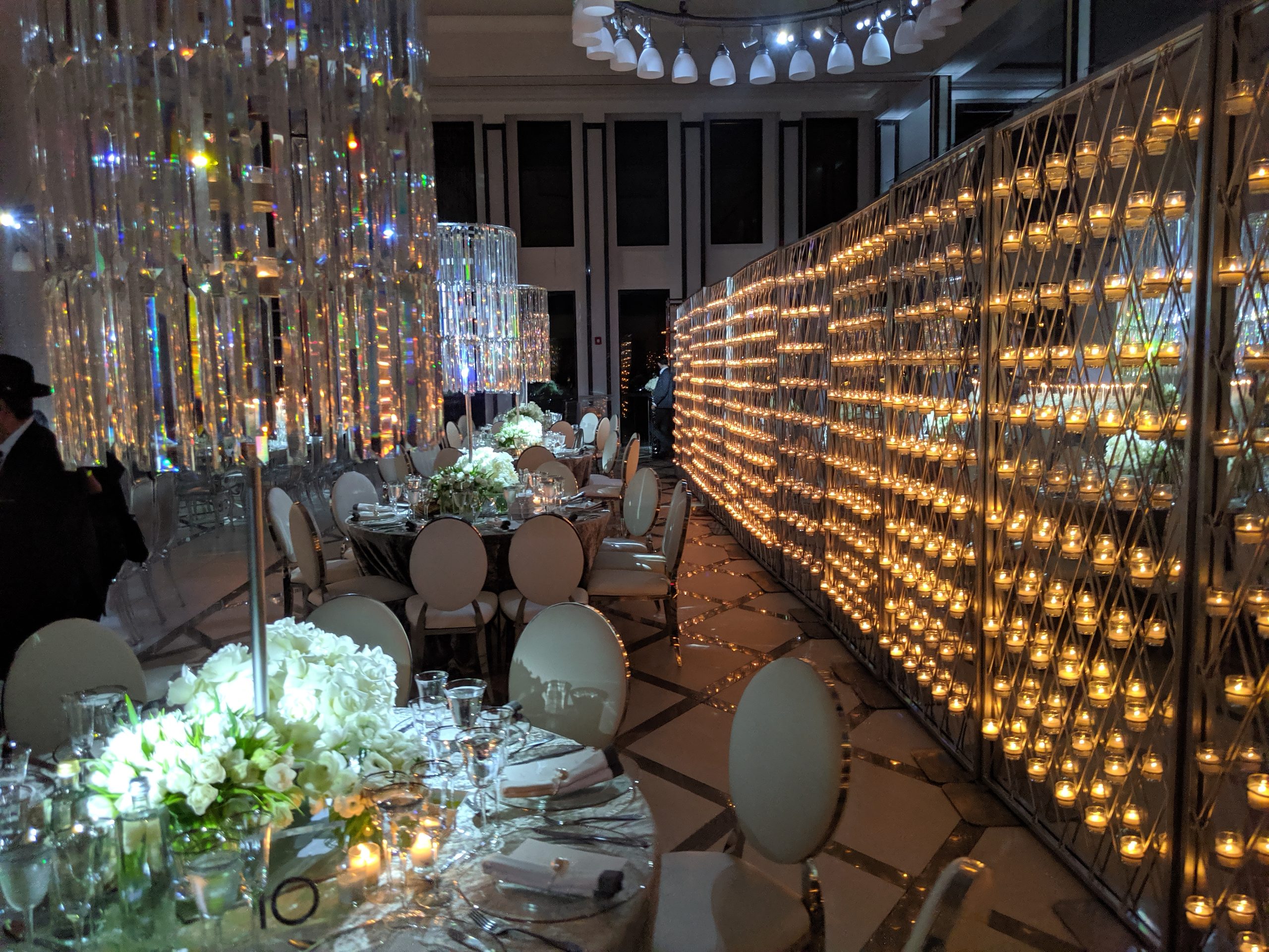 A wall of hundreds of candles down the length of the room, round tables set in white beside it, a crystal chandelier above