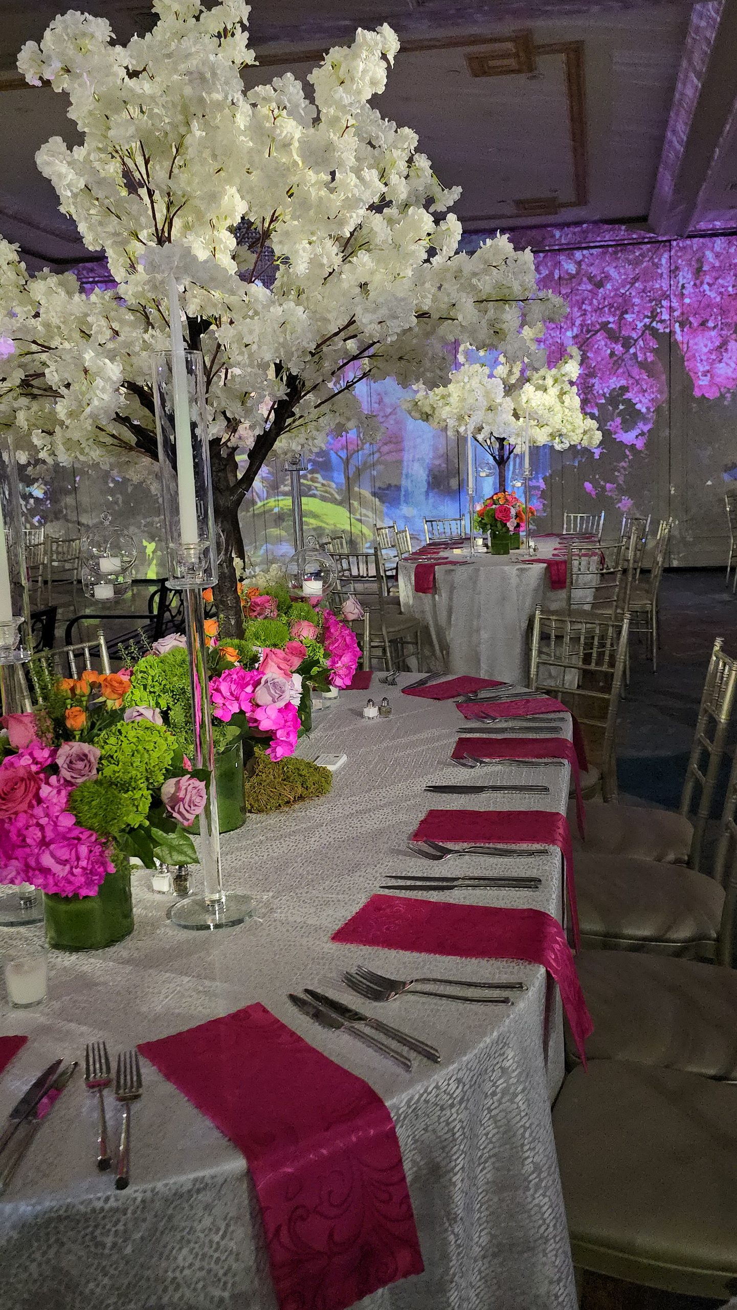 A white blossom tree over a set table, the projected blossom forest and waterfall on the wall behind