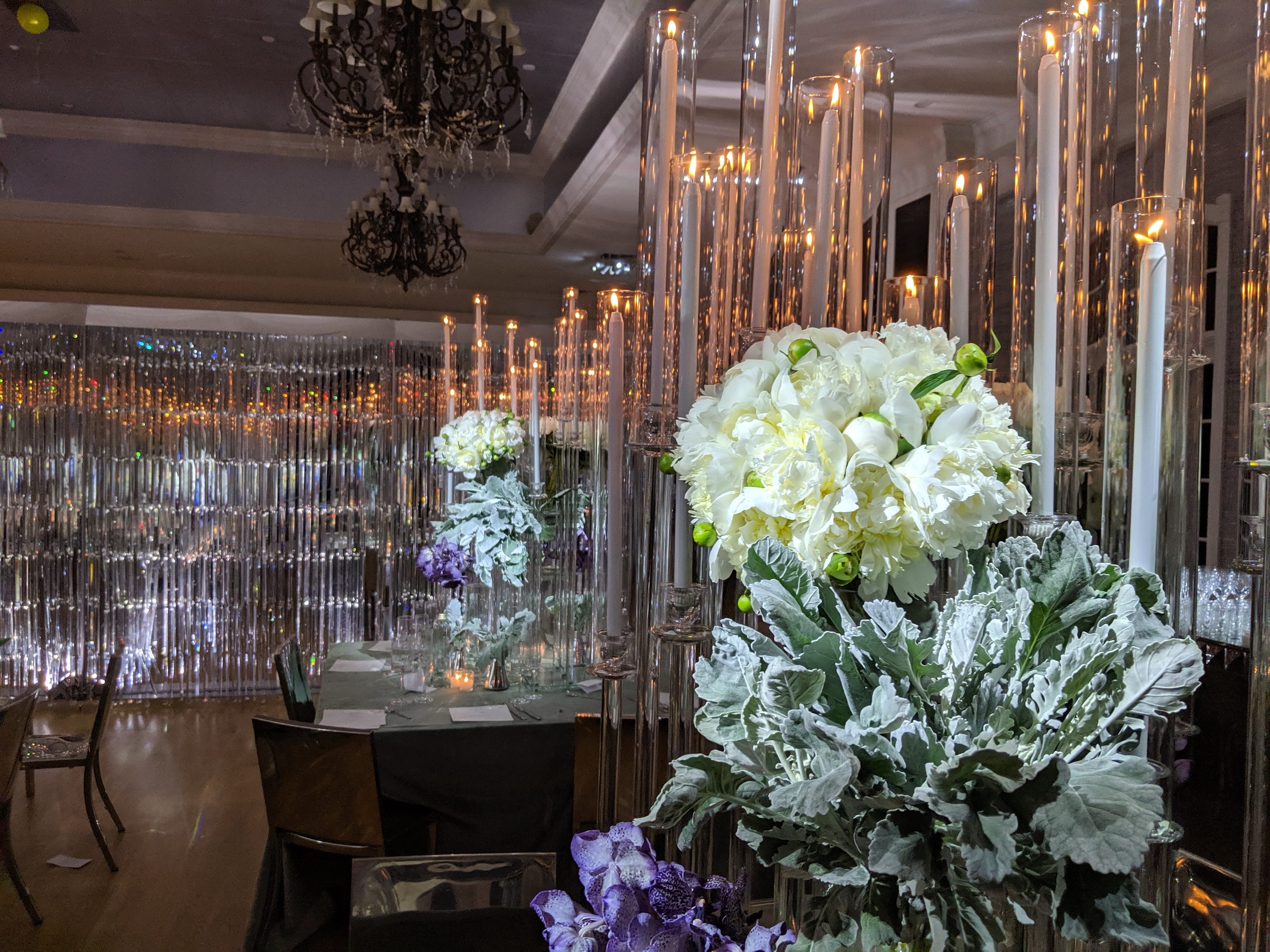 White orchids close, tapers above them, the chandelier and the lit crystal beyond