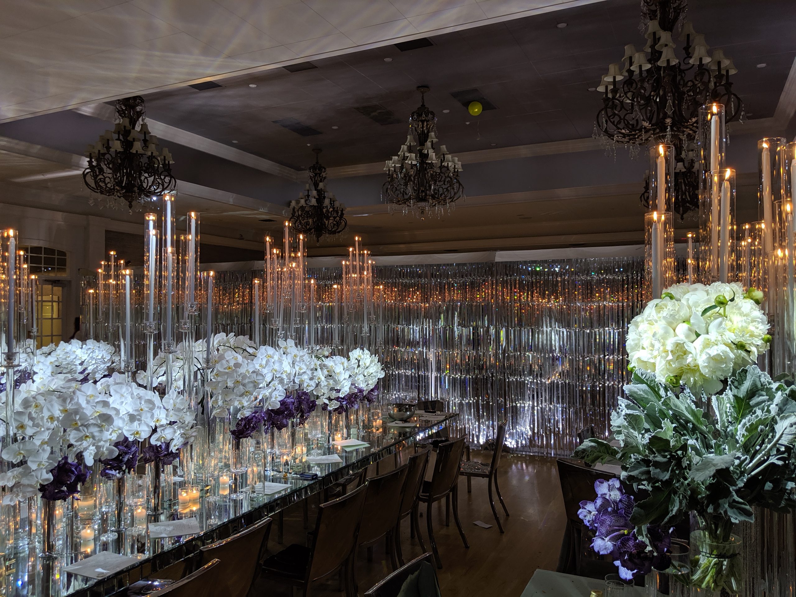 A long mirrored table under tapers, white orchids and purple down its length, the crystal wall behind