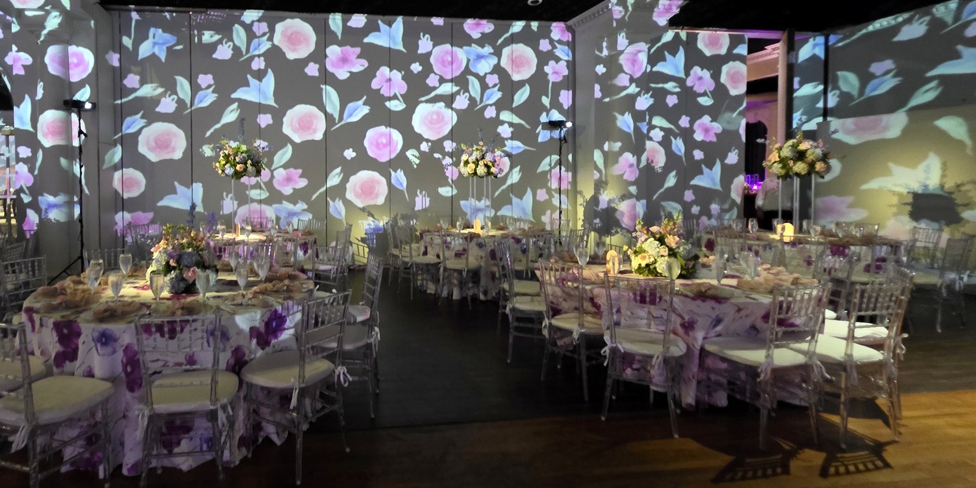 The whole room under projected florals: the long tables, the dance floor, every wall in bloom