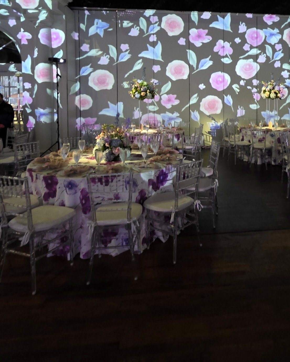 A room wrapped in projected watercolour florals, a pink-lit storefront at the far end