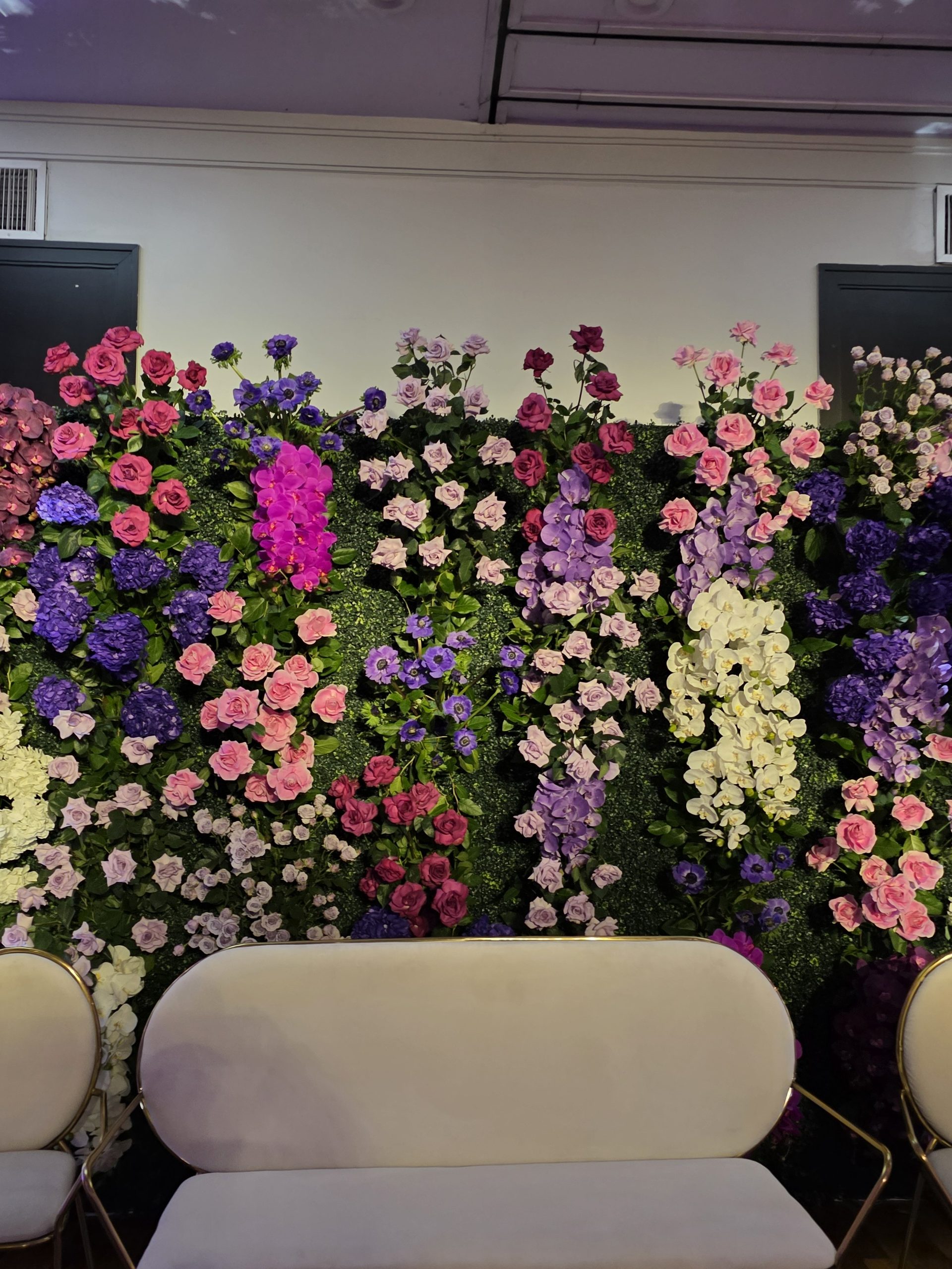 The flower wall and the white sofa in front of it, the room lit violet