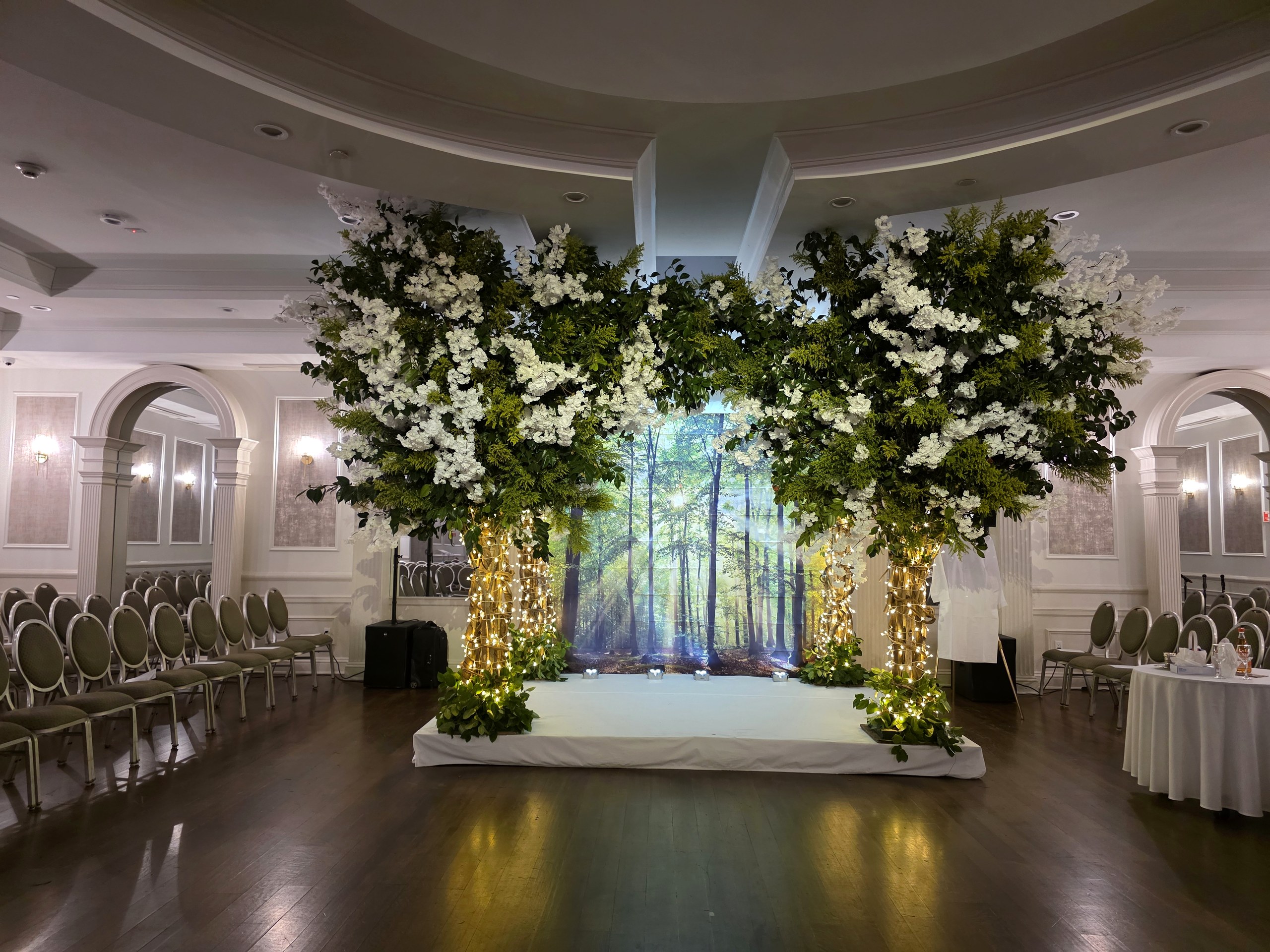 The chuppah between two flowering trees, a sunlit forest projected behind it