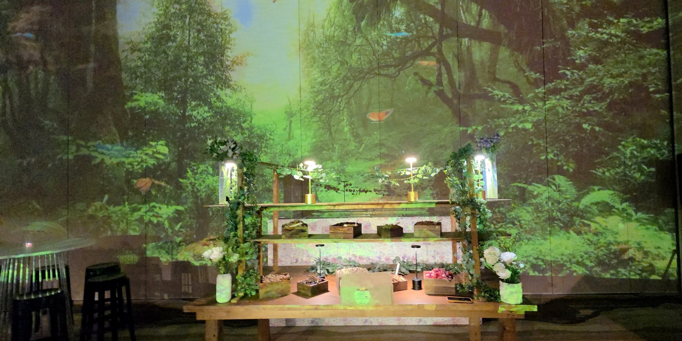 The forest projected across the whole wall, the timber bar dressed in greenery in front of it