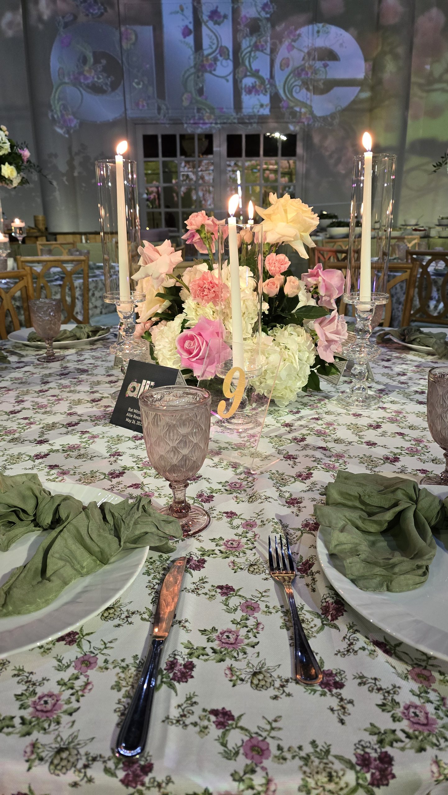 Candles and roses on floral linen, the projected gate and the girl's name on the wall behind
