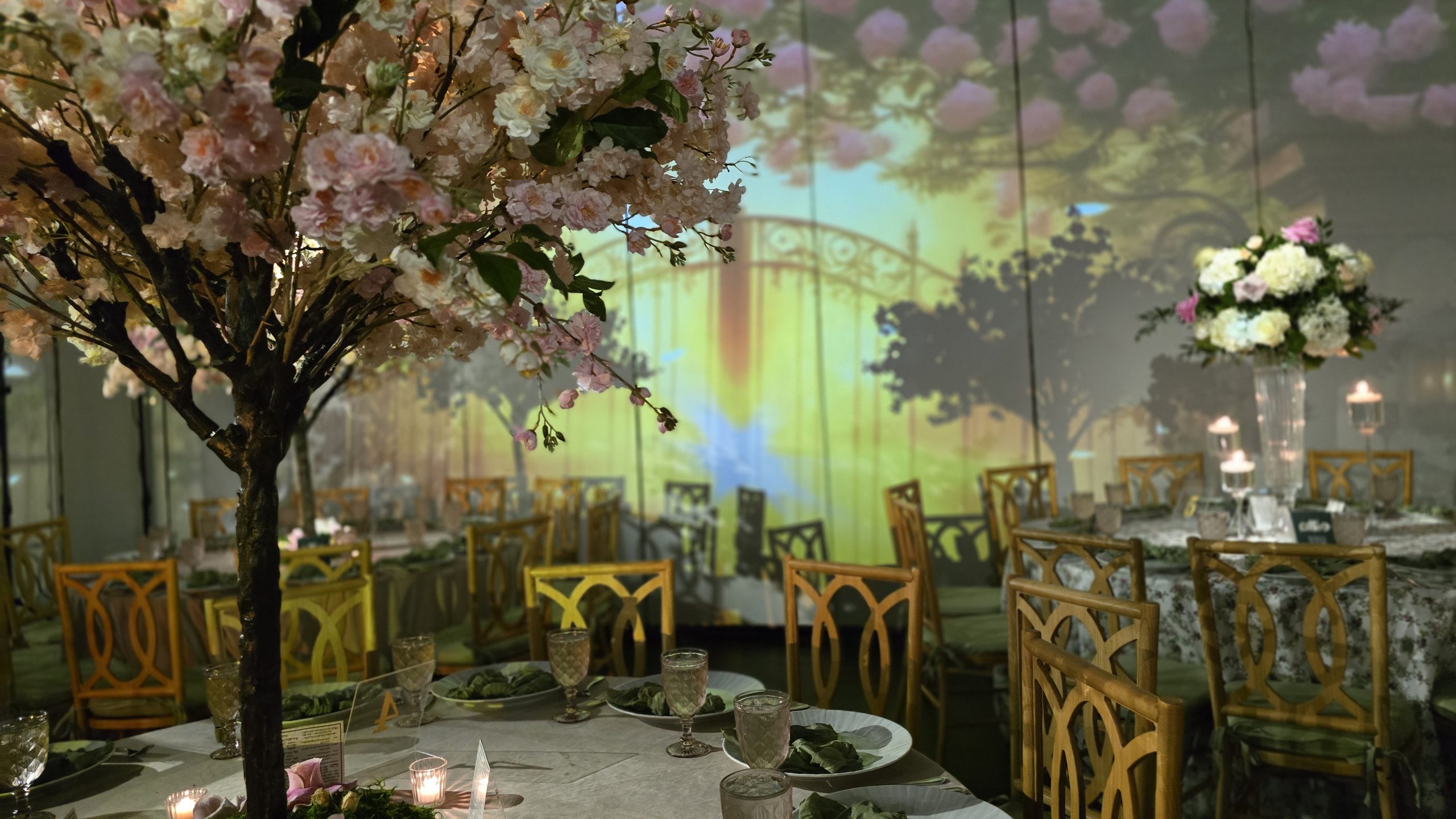 A blossom tree over a table set with floral linen, the projected garden behind