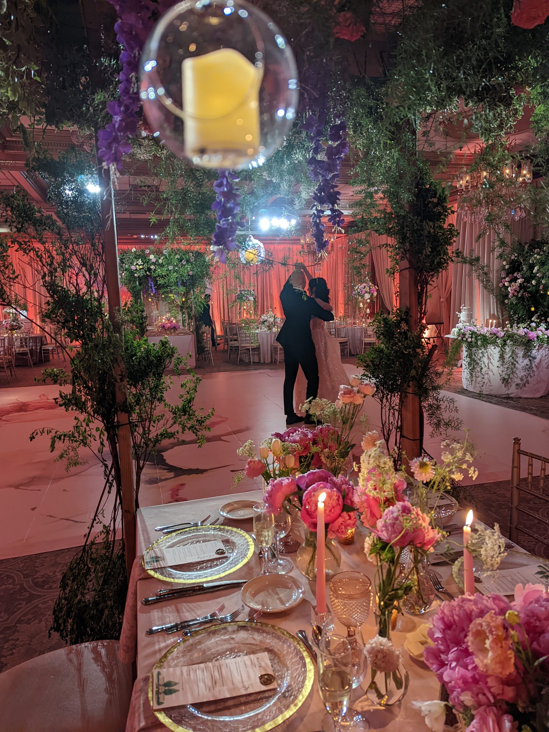The glass house of trees, lit warm, the long table in front