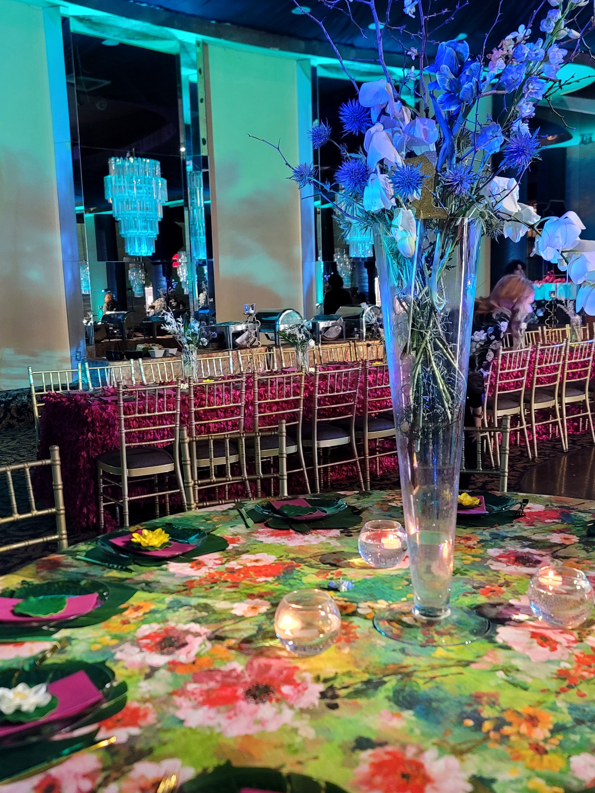 Blue florals over the painted tablecloth, the chandelier reflected in the mirrored wall