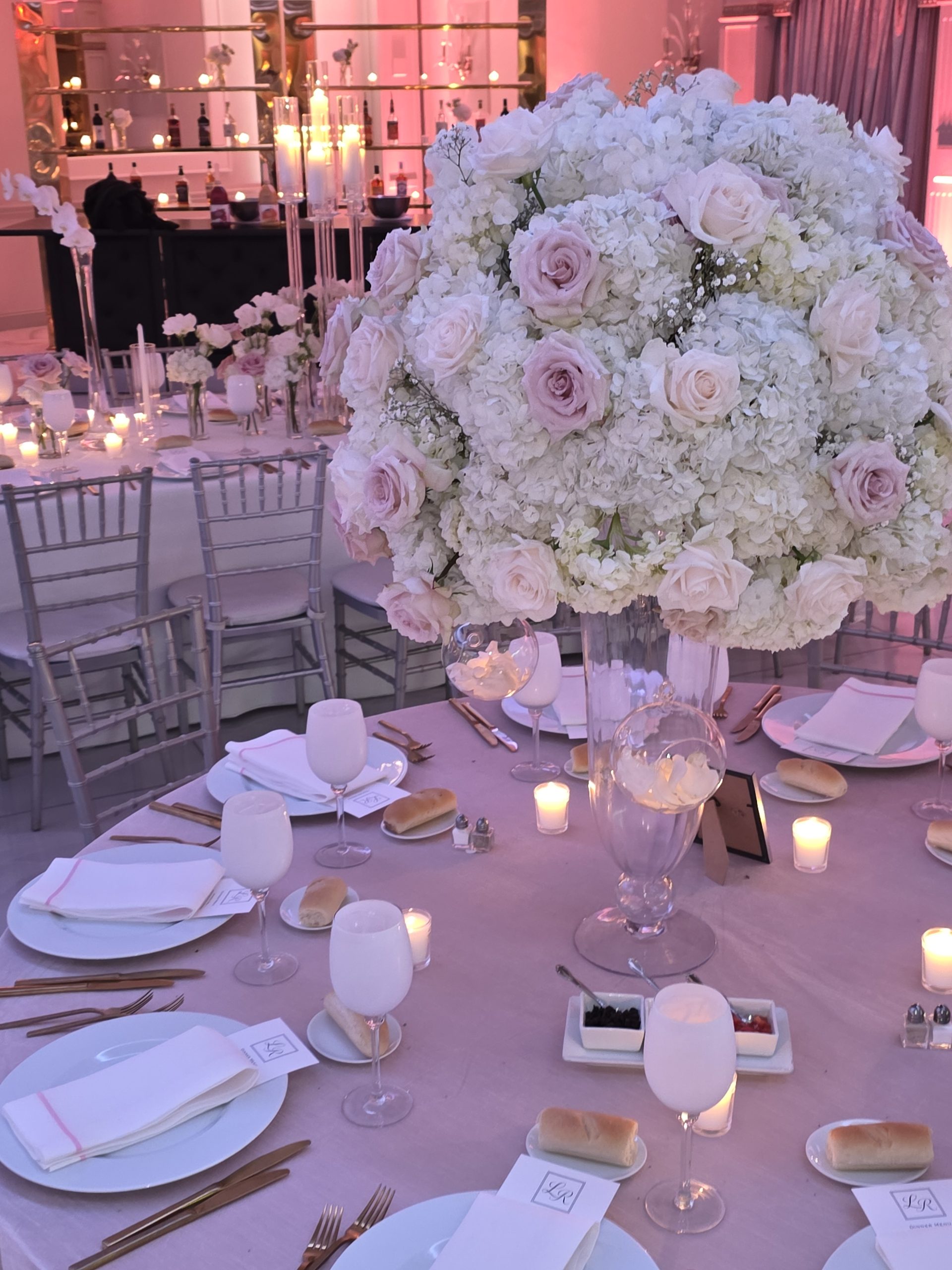 Blush roses and hydrangea on a tall glass stand, candles and gold cutlery below