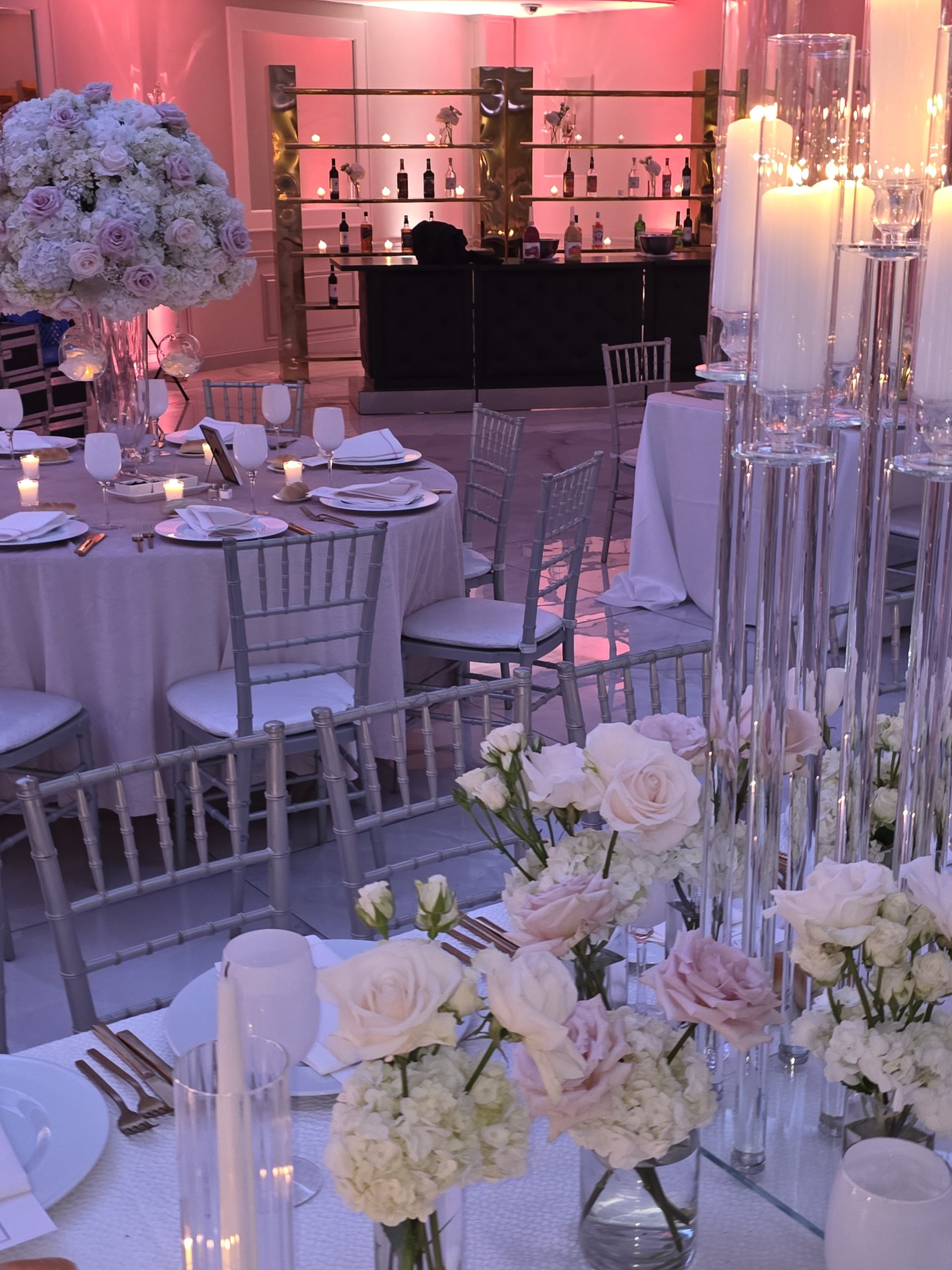 Round tables set in white and gold under tall candles, the bar lit rose behind