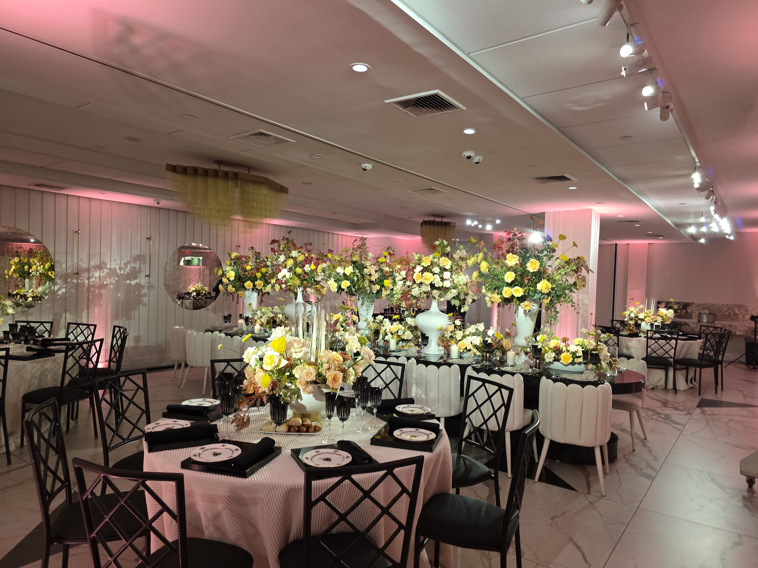 Round tables and black chairs under the pink light, roses at the centre