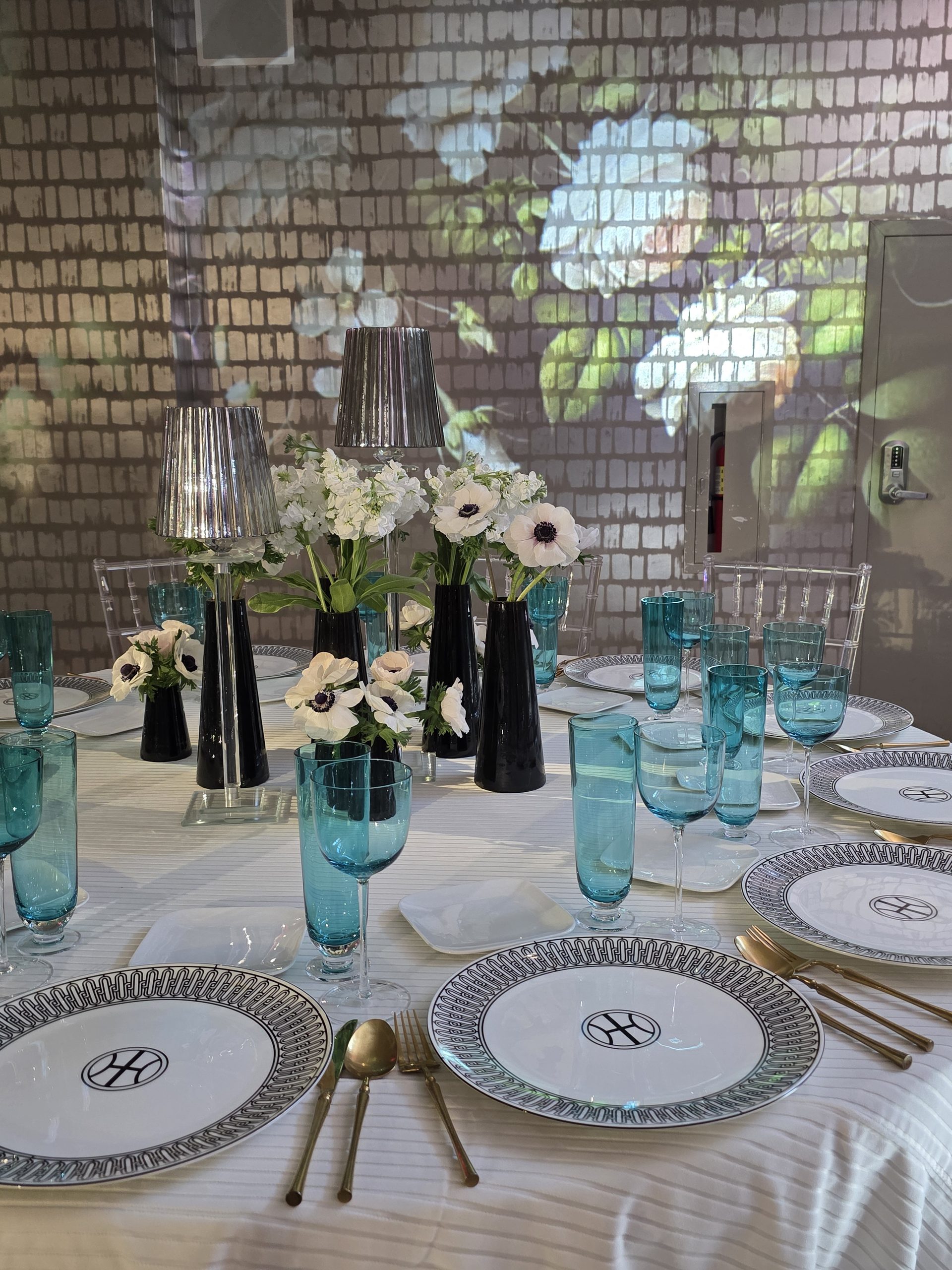 White anemones in black vases, teal glasses, the projected hydrangea behind