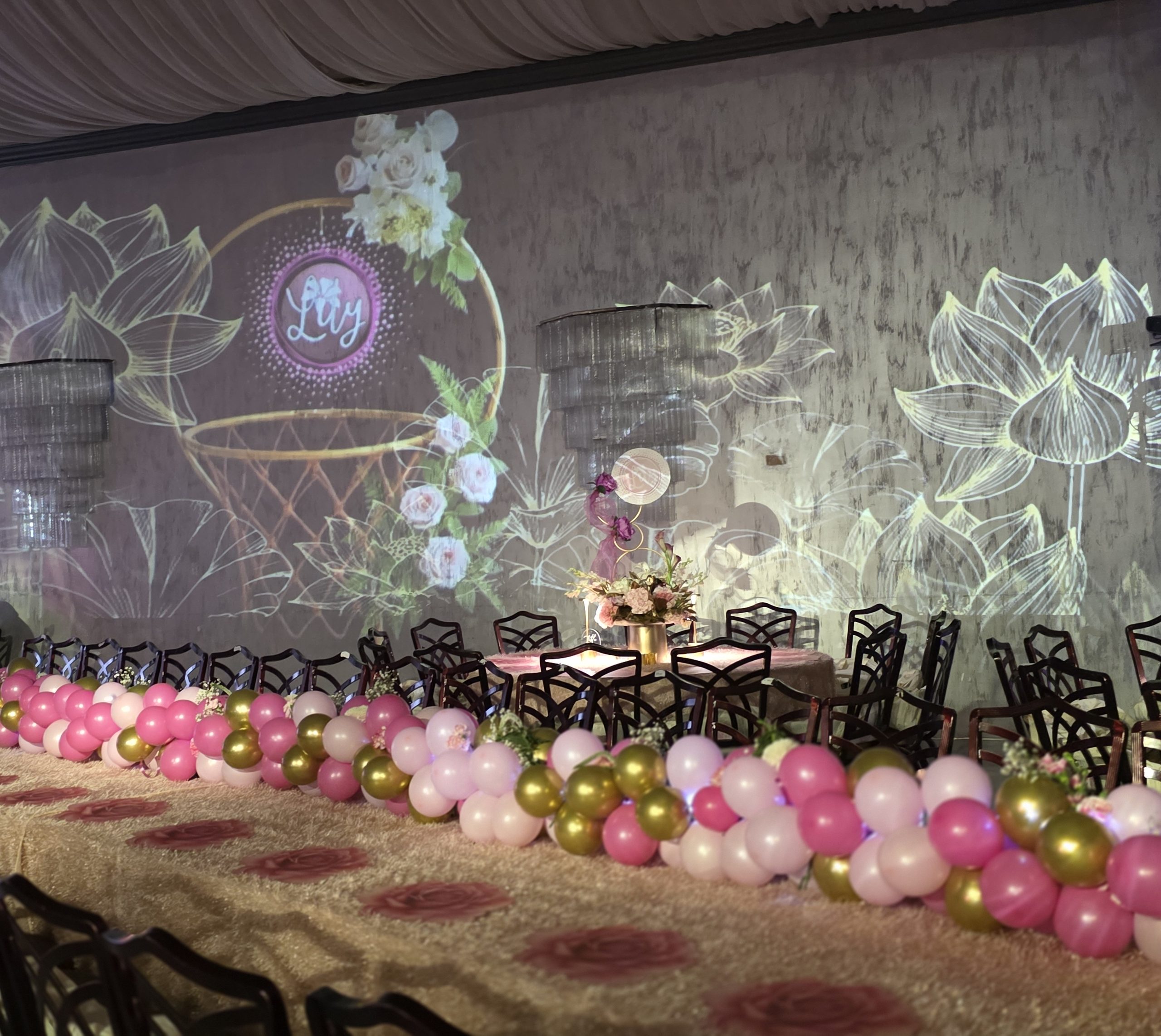 The projected monogram on the wall, pink and gold balloons beneath