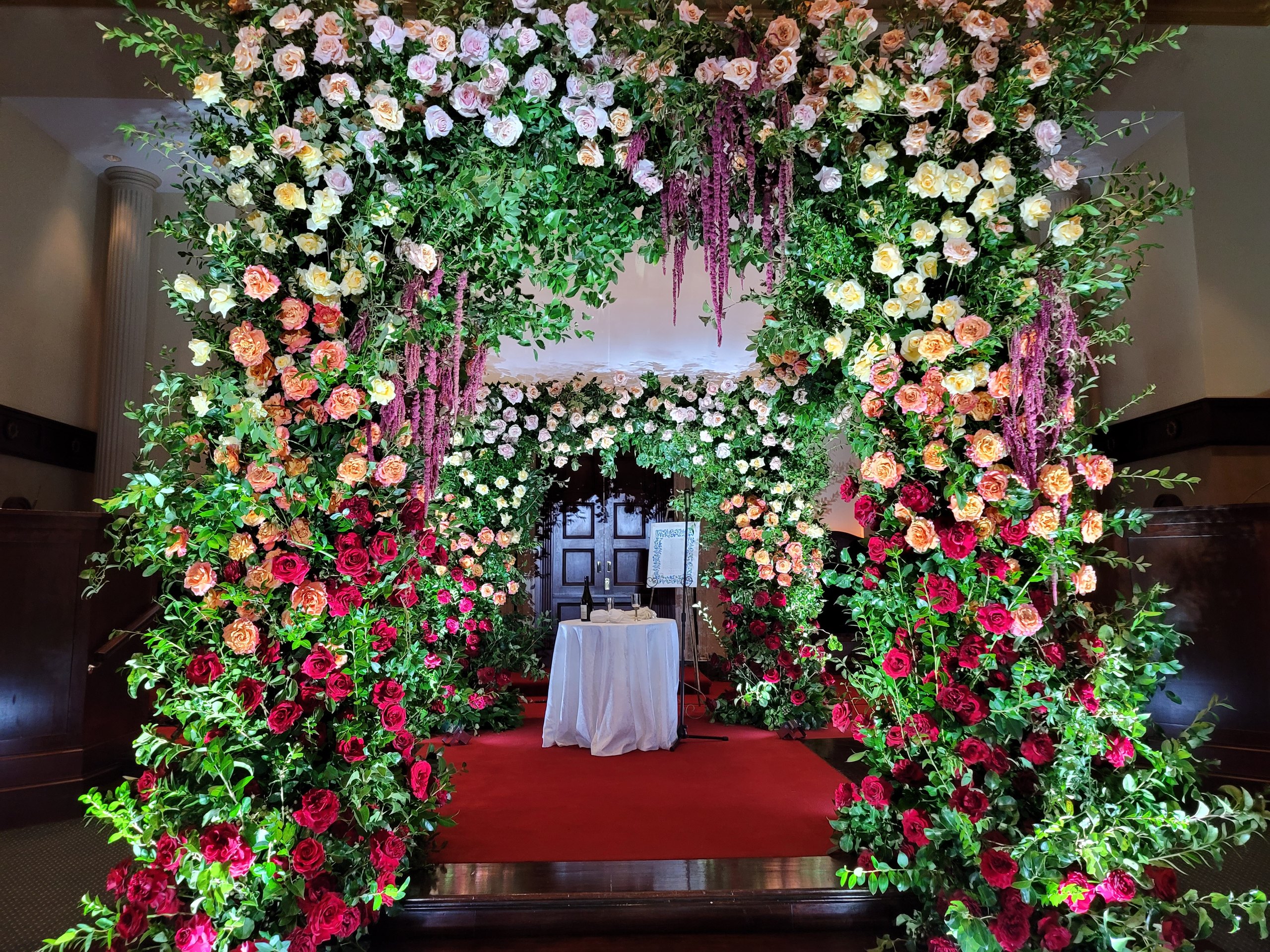 The rose chuppah whole: the arch, the carpet, the wood-panelled room behind it