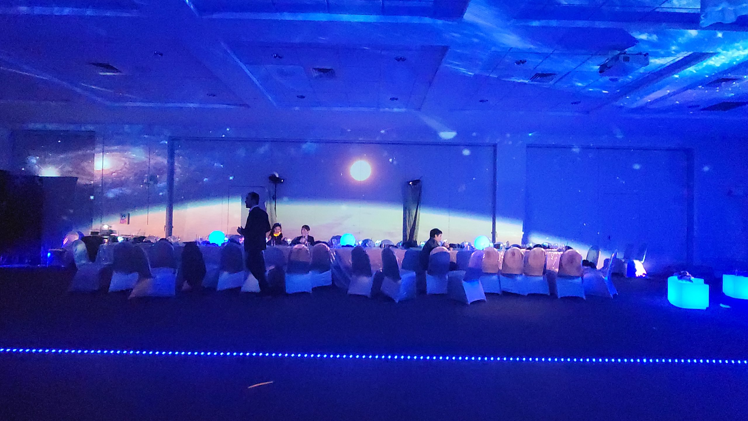 A planet rising over the horizon, projected wall to wall above the set tables; the ceiling a galaxy