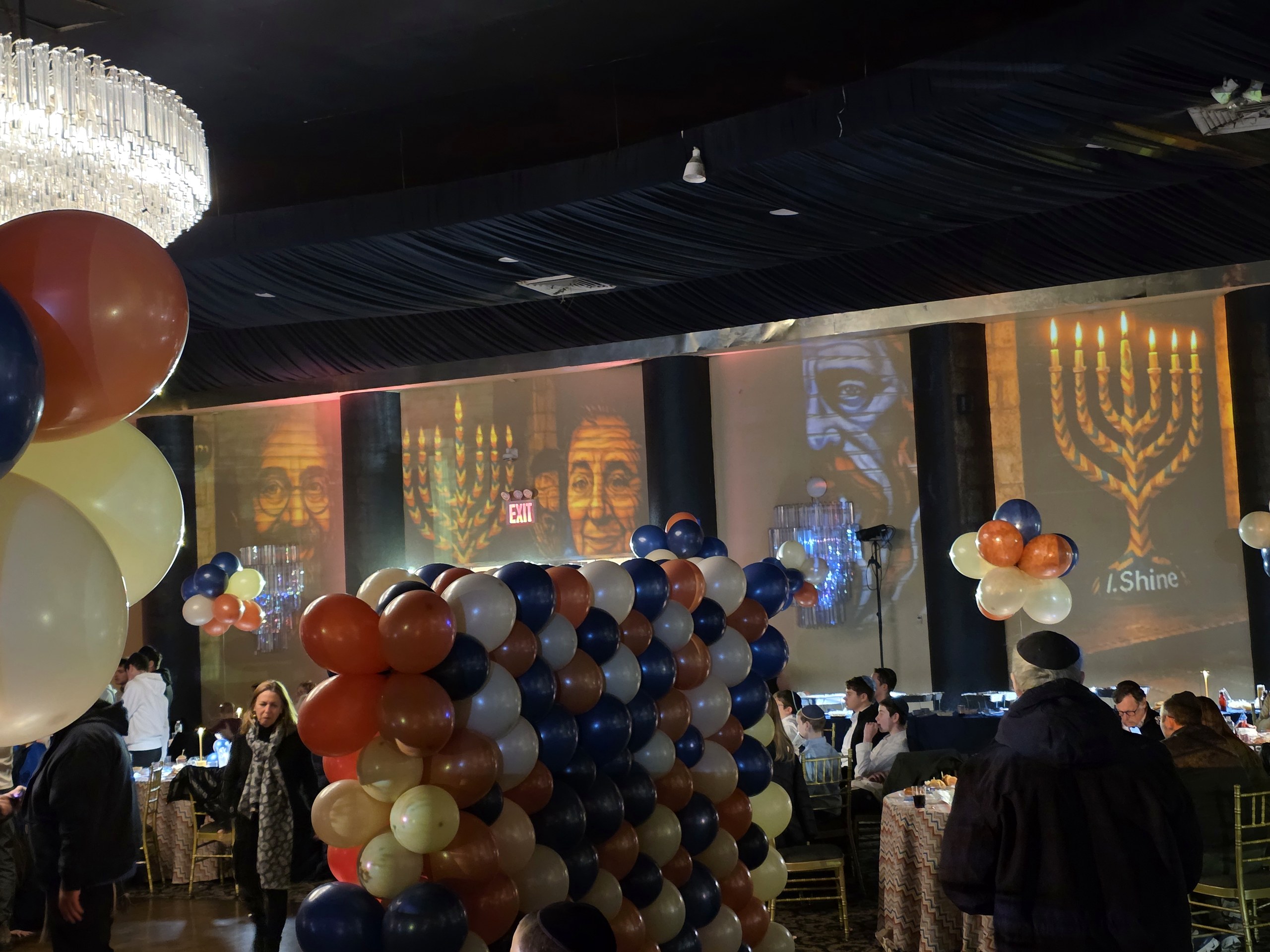 A Chanukah party: a menorah projected on the wall, balloons, the tables set