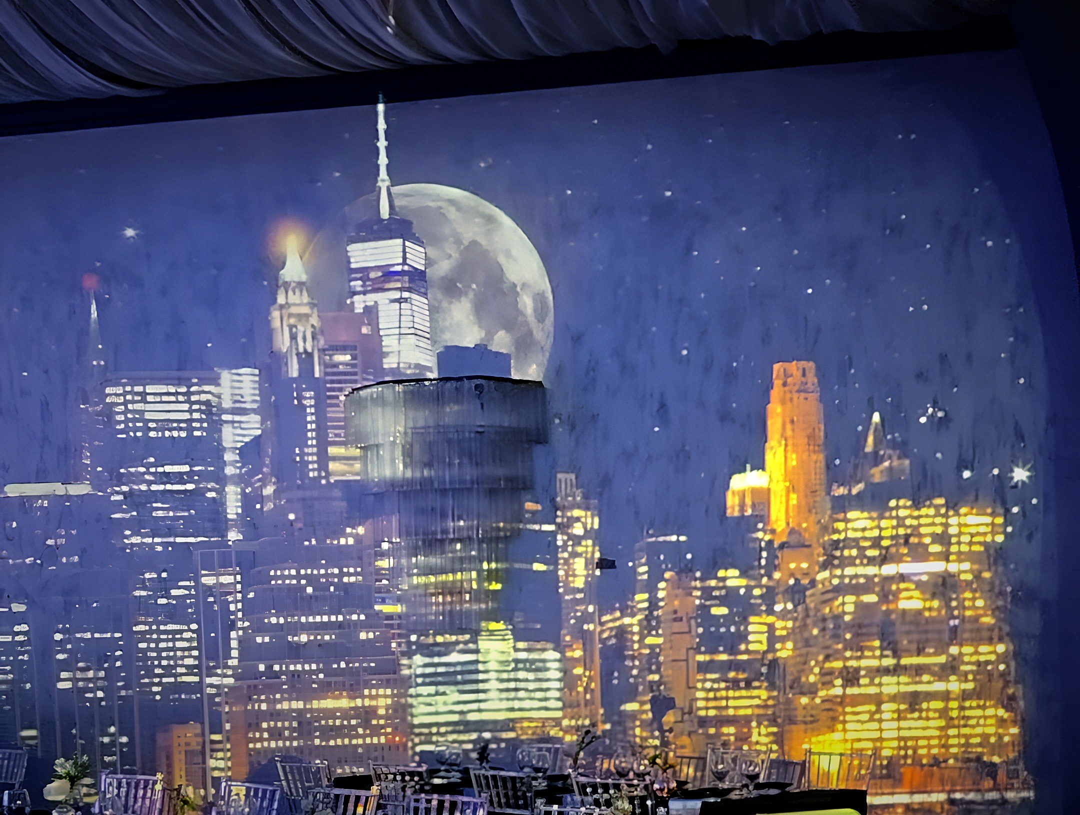 The whole back wall over the set tables: the city at night, the moon, the chandelier