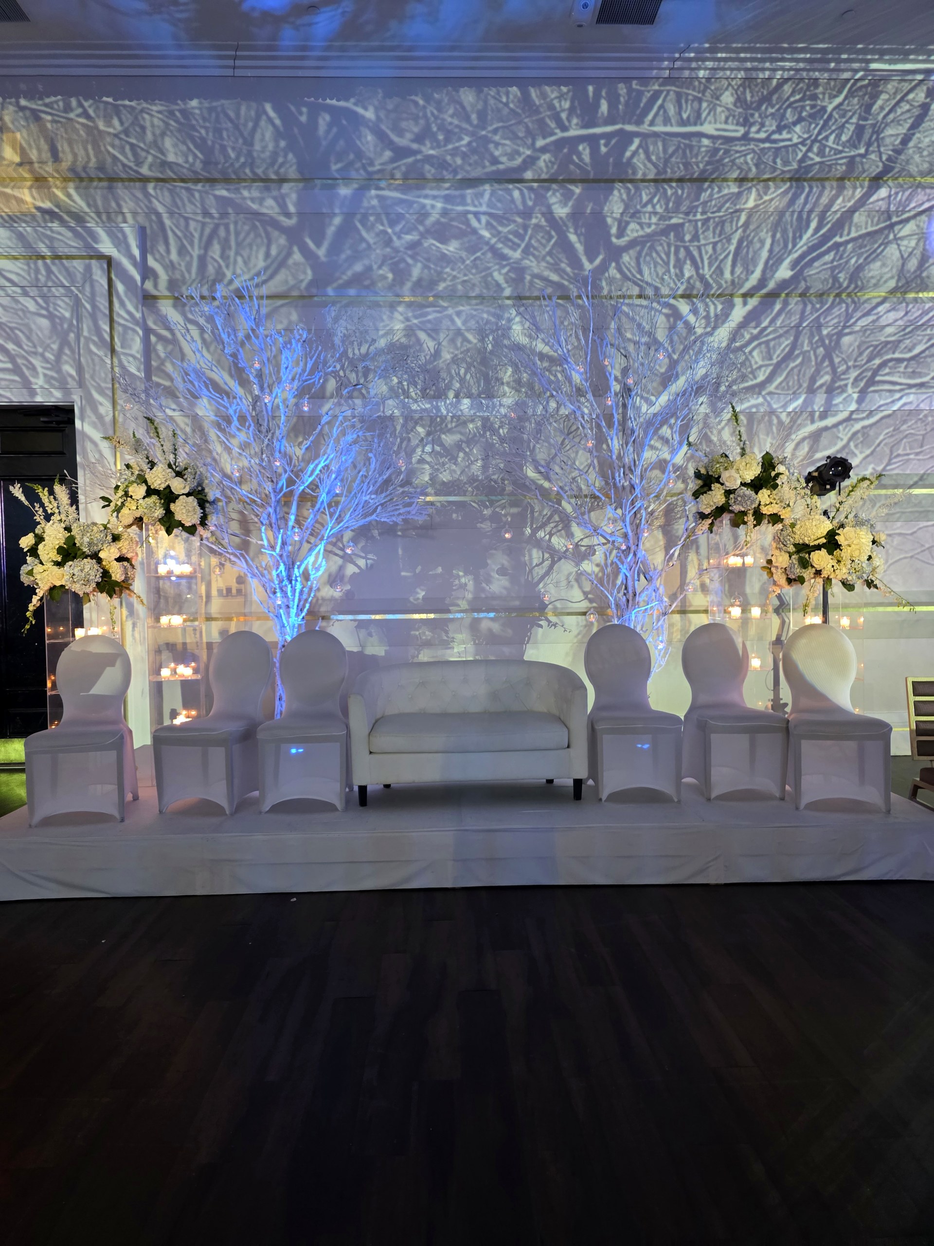 A projected winter forest across the wall behind the white lounge and florals