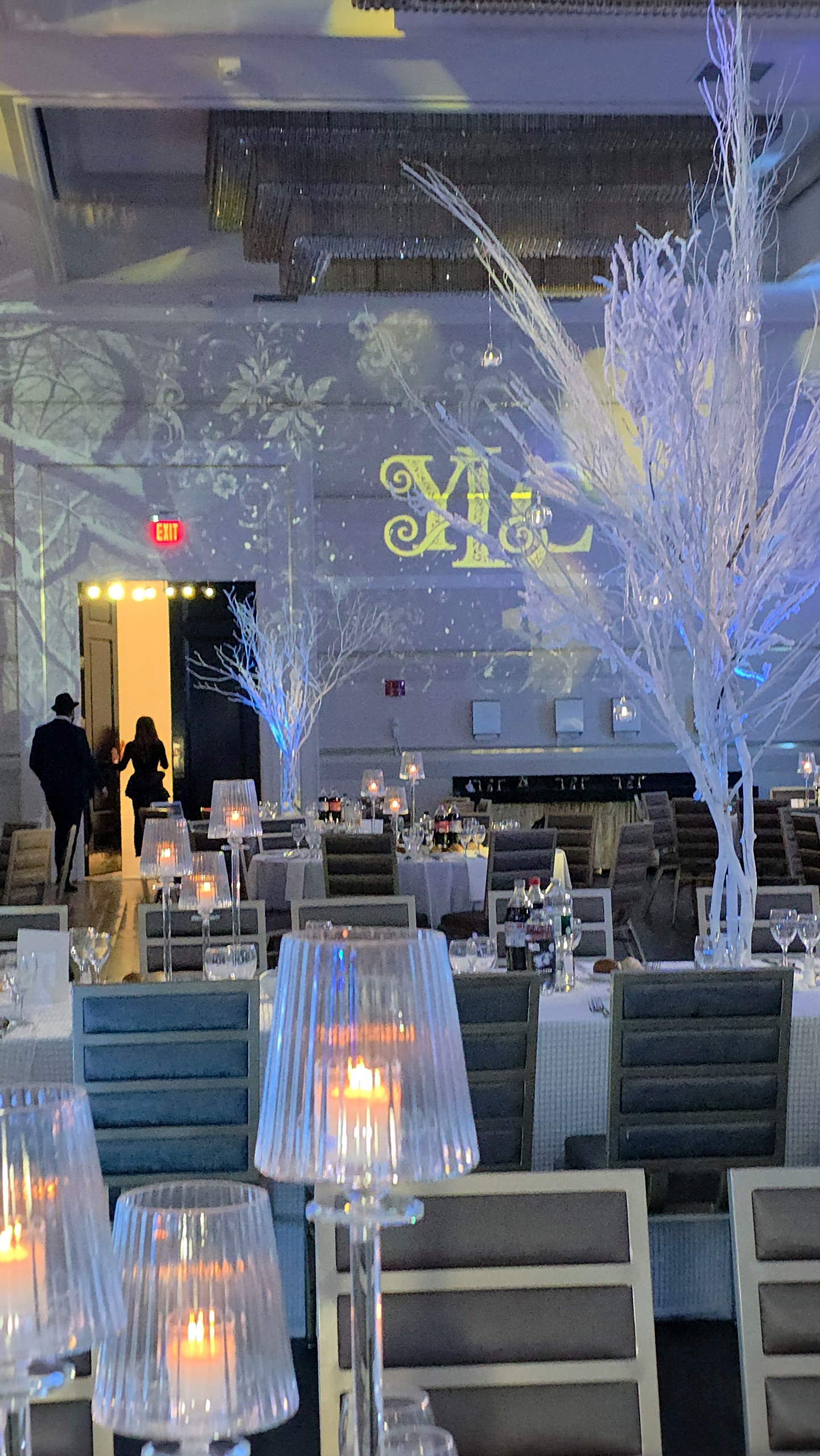 The tables under white branches and the projected forest, the couple's monogram on the wall