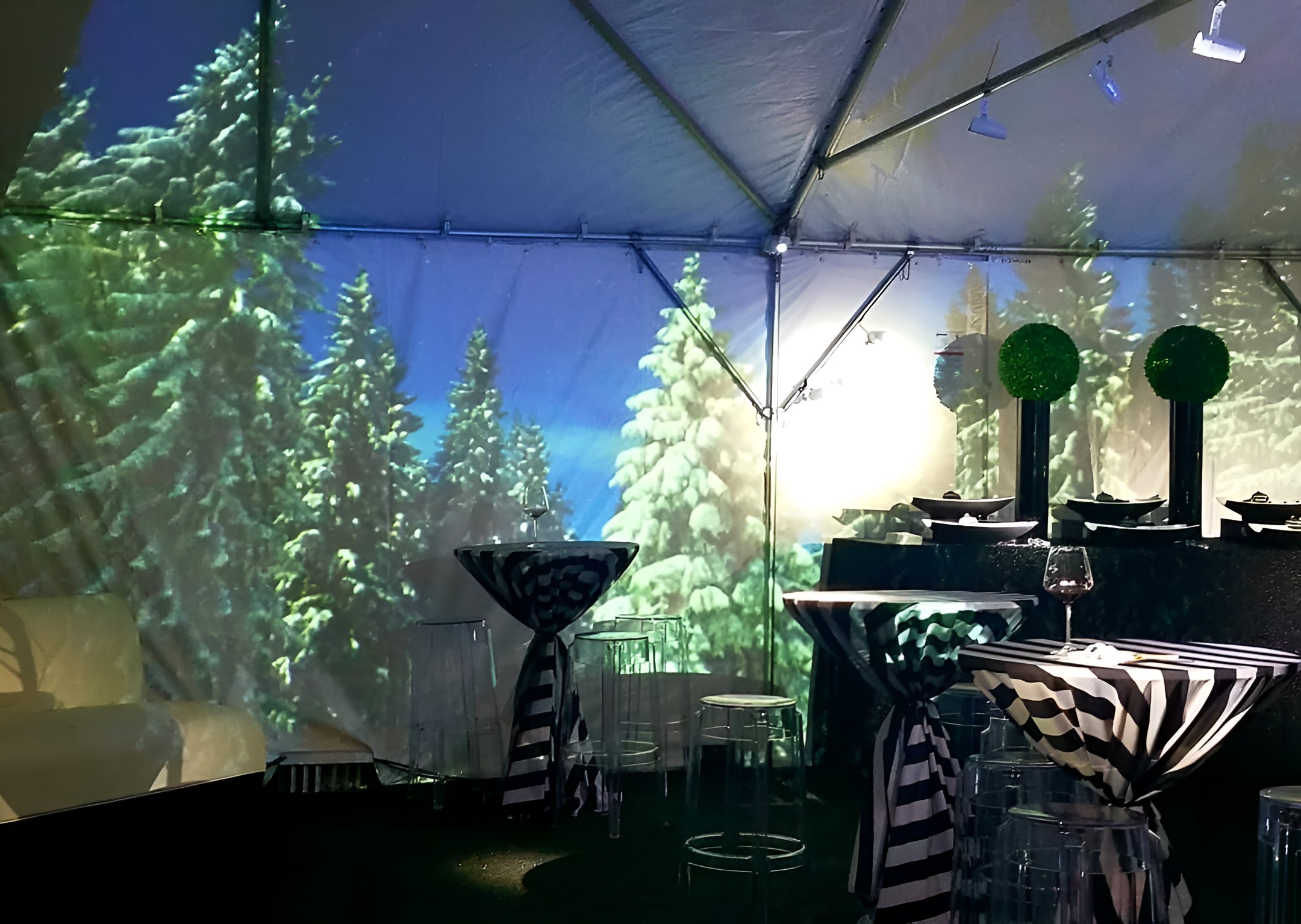 Snowy pines projected onto the inside of a tent, cocktail tables in front