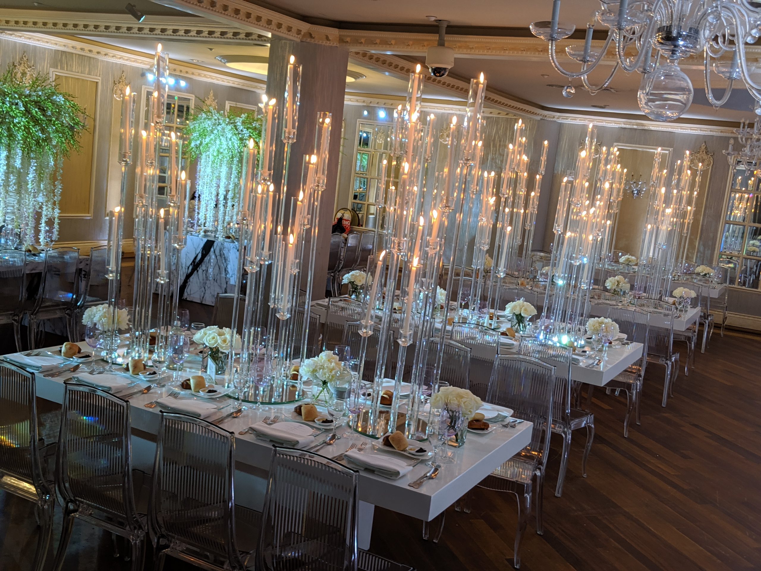 Tall glass tapers lit down a long white table under green wisteria