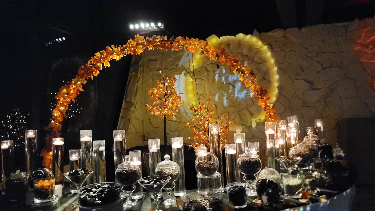 A gold floral arch over a long table of candles in glass