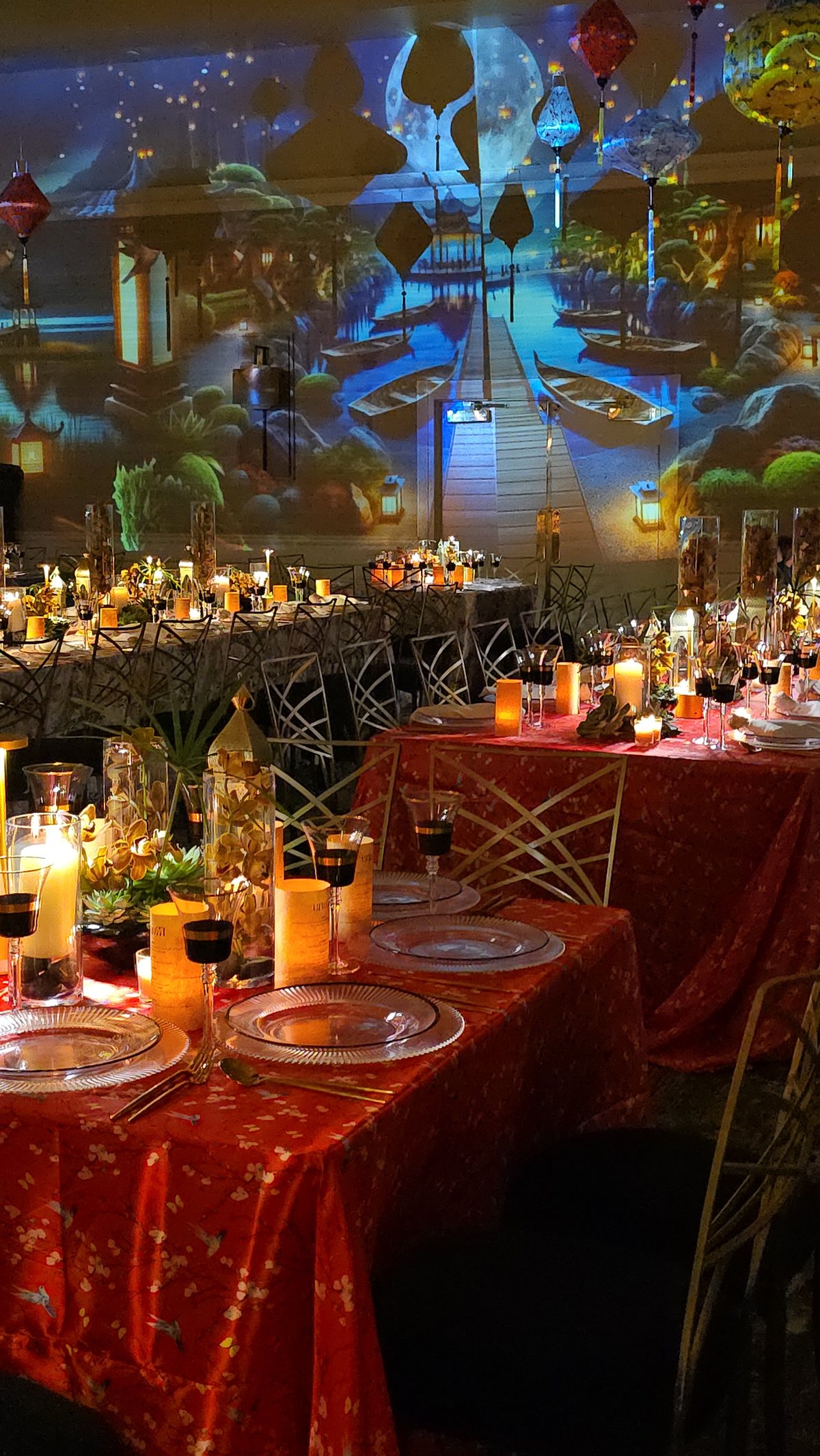 Candlelit tables on red cloth under hanging lanterns