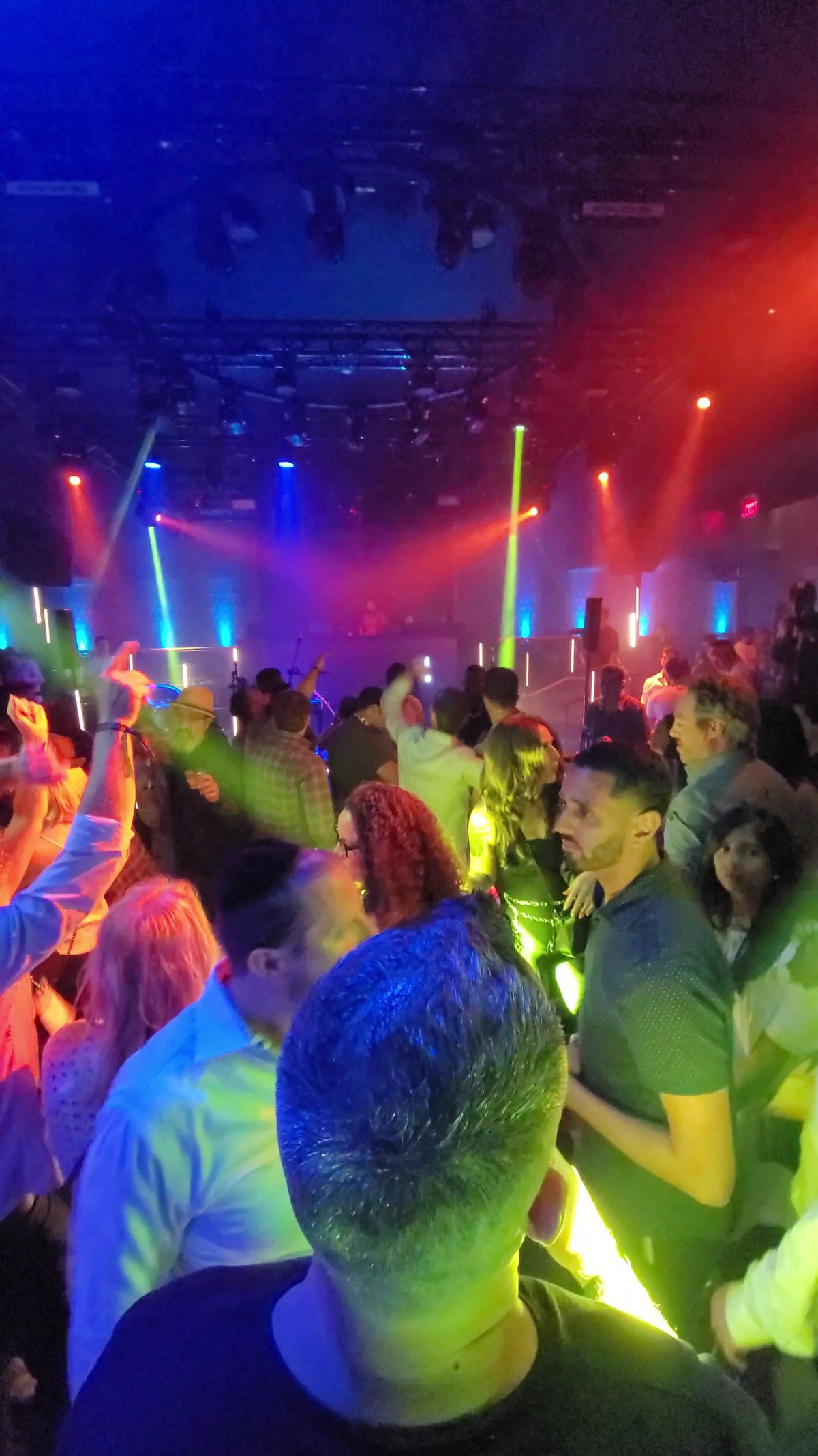 A packed dance floor under green and red beams