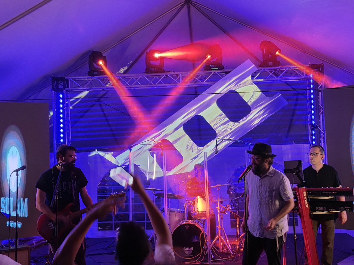 The band on stage under truss lights and red beams
