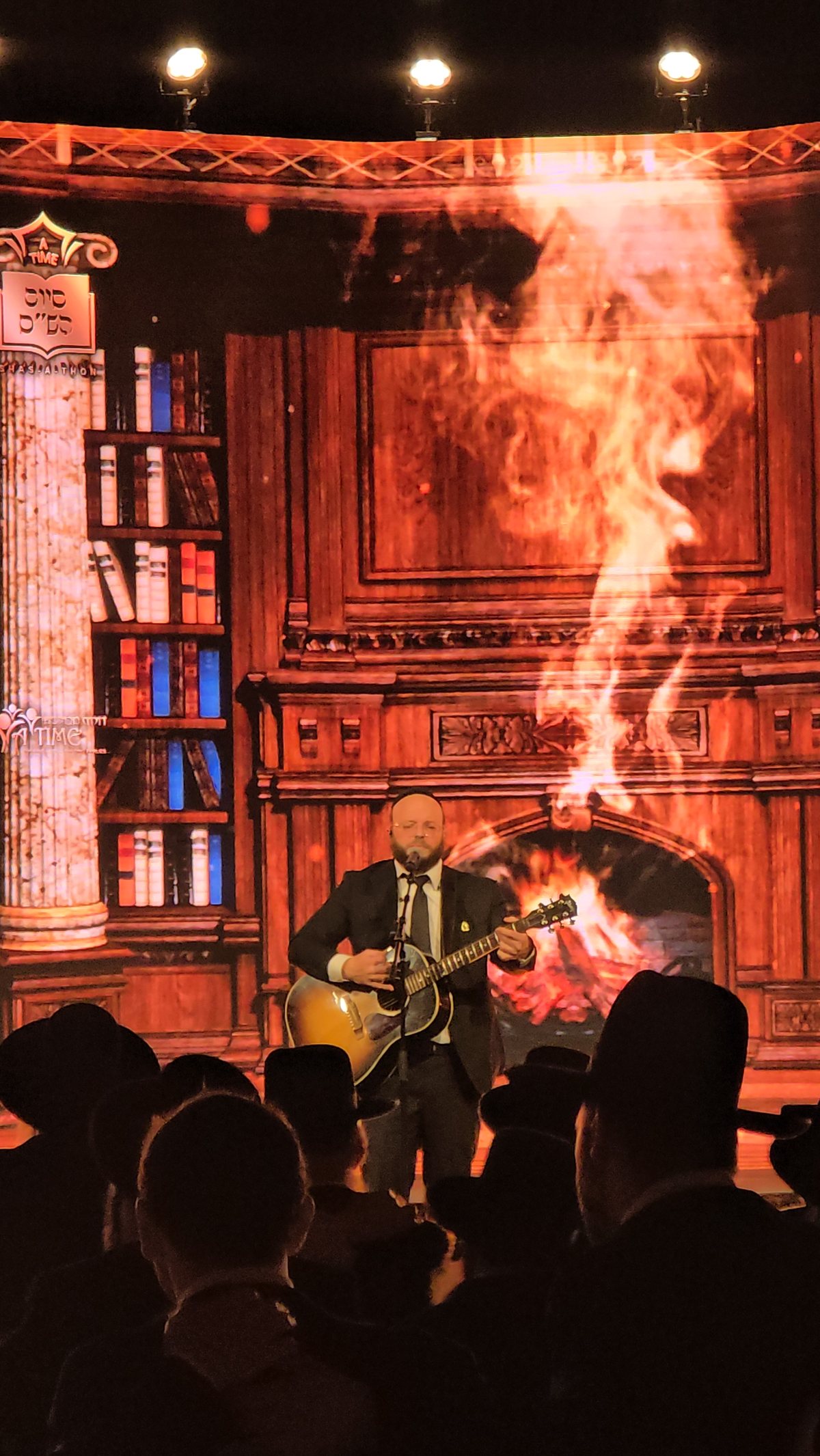 A library and fireplace projected behind the singer on stage
