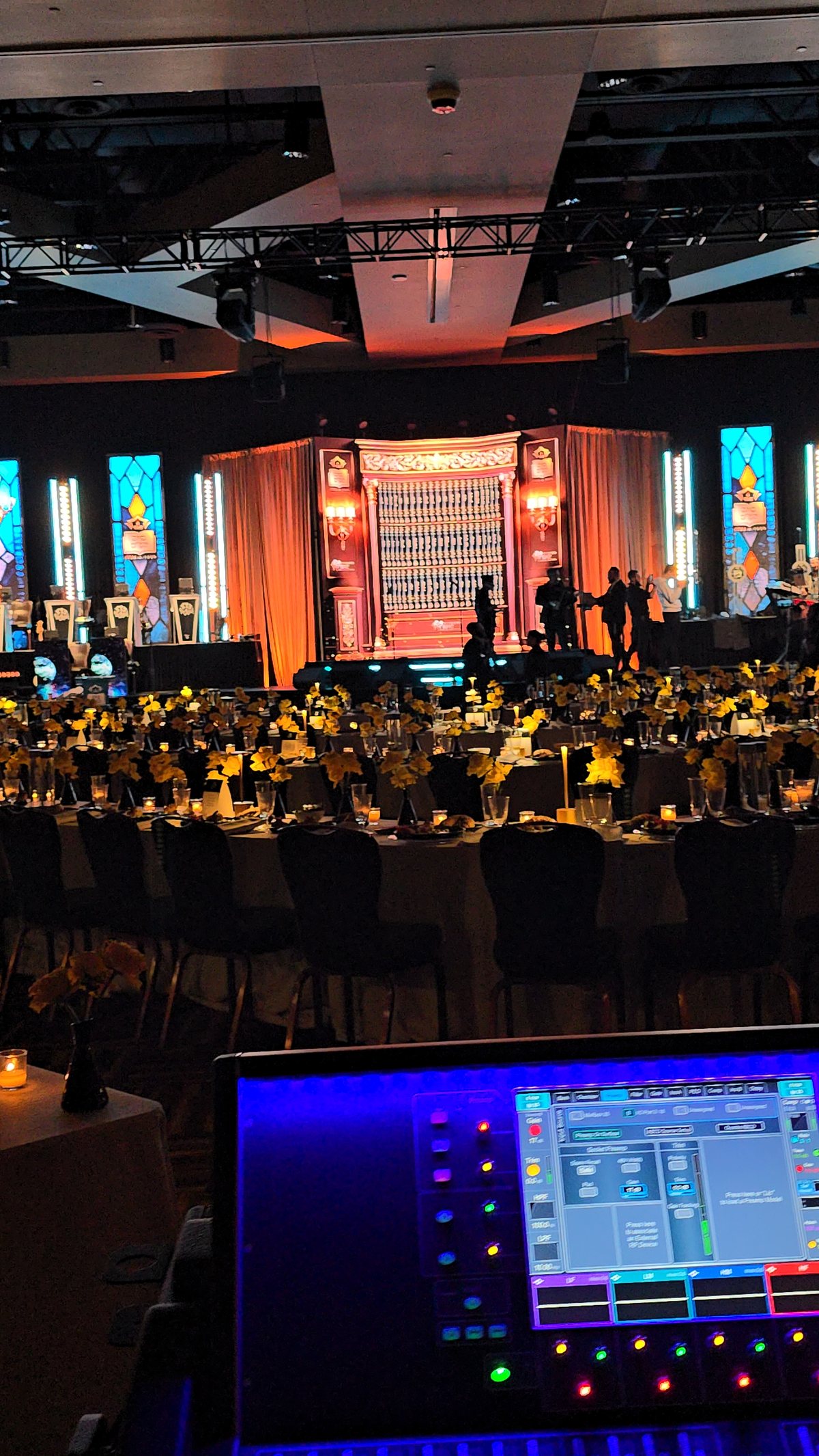 A gala ballroom lit warm, the stage glowing behind the tables