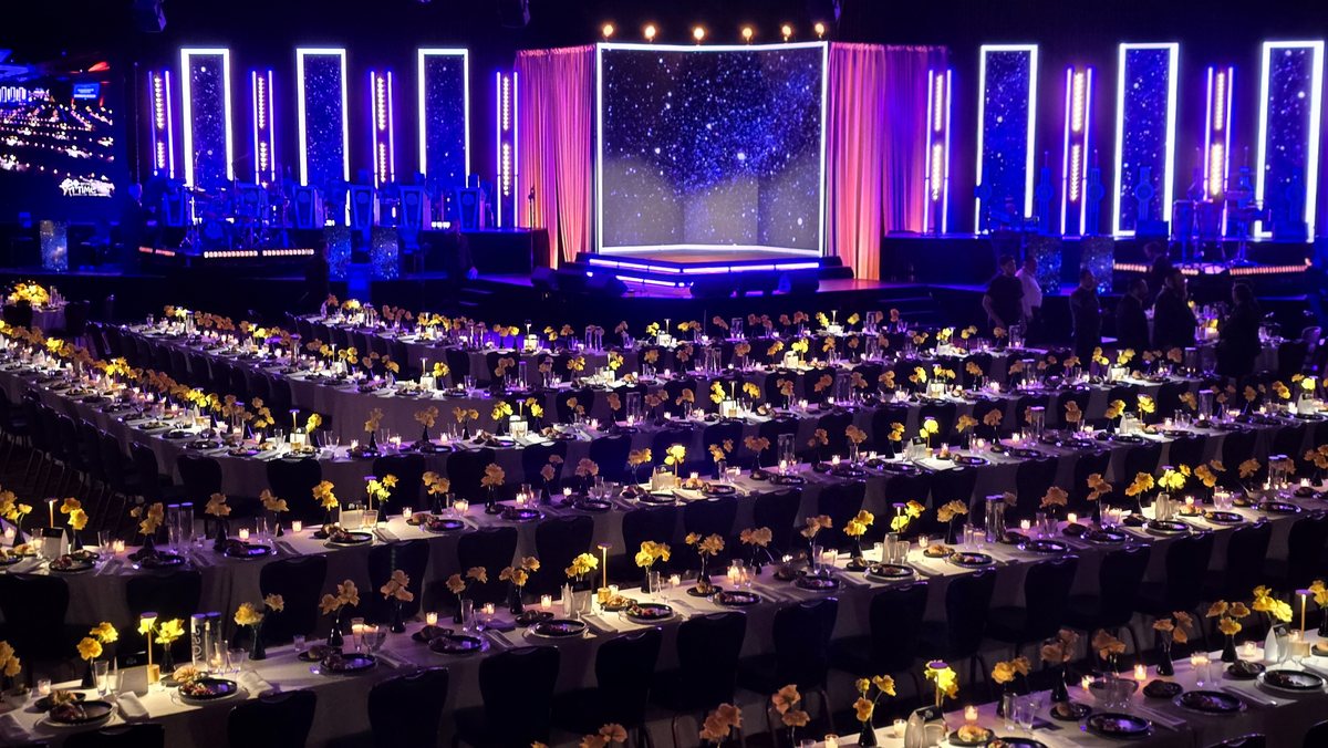A deep-blue gala ballroom, a starfield on the stage over candlelit tables